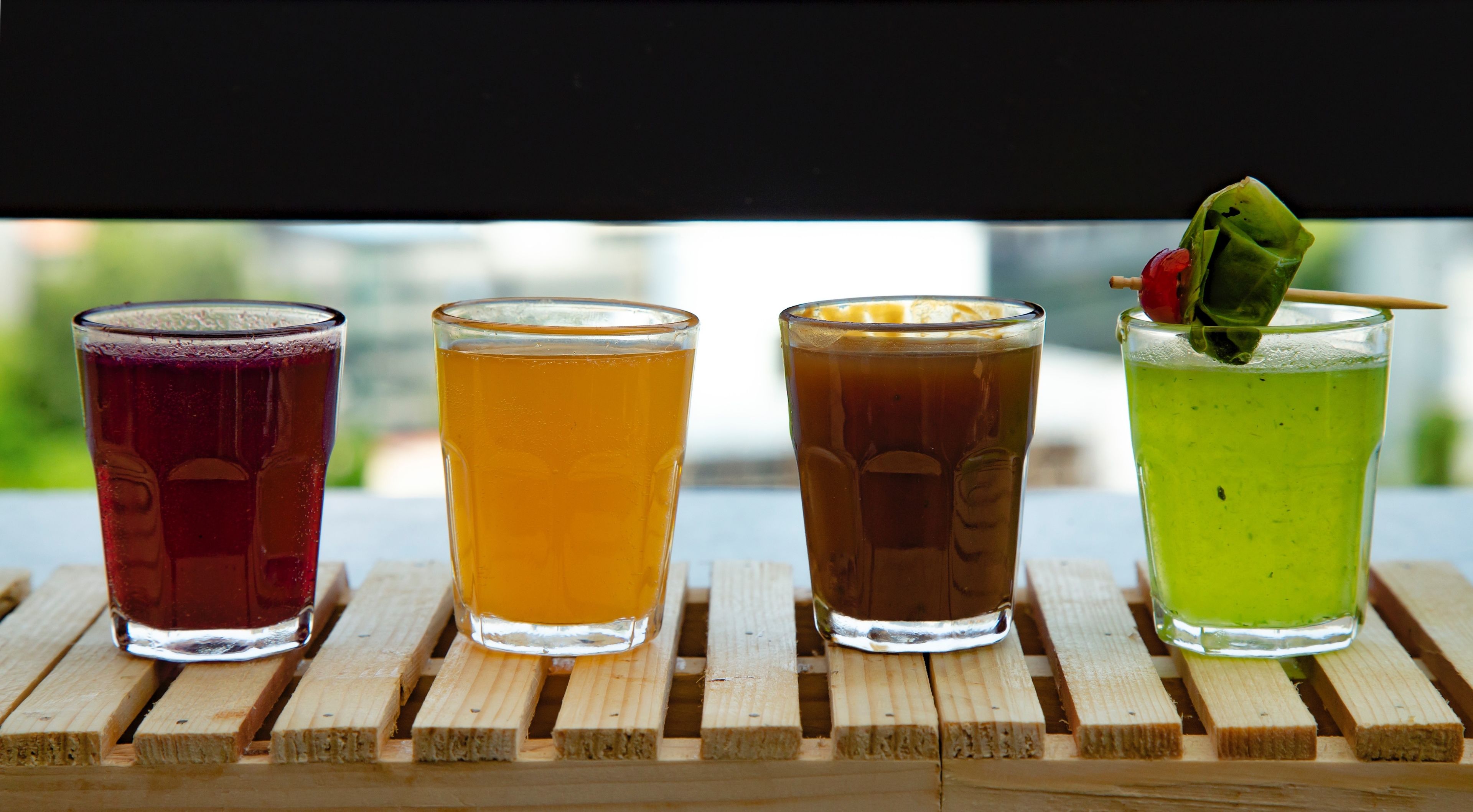 Four glasses of different beverages on a wooden surface.