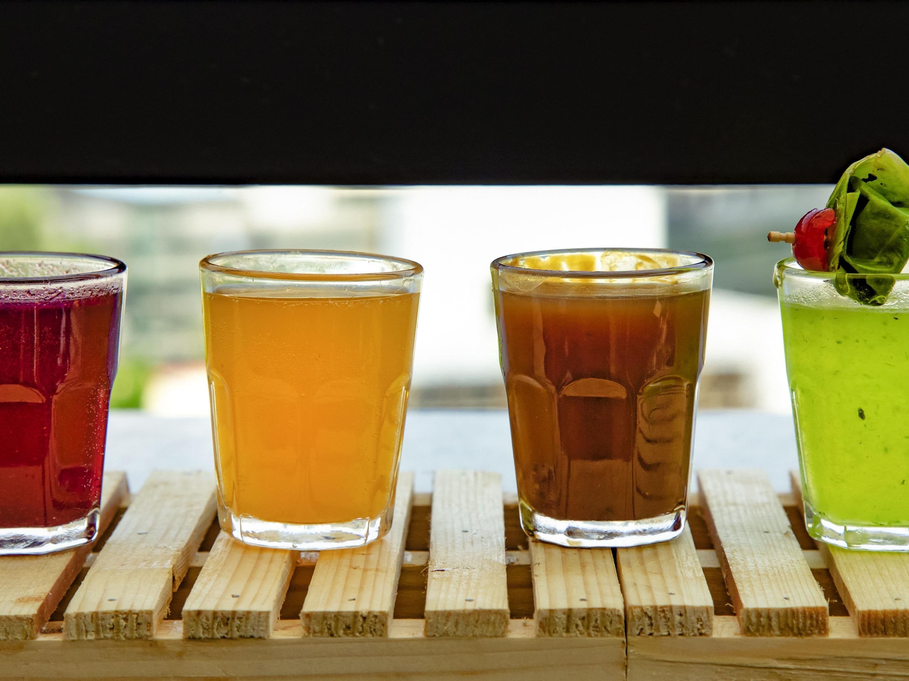 Four glasses of different colored beverages on a wooden surface.