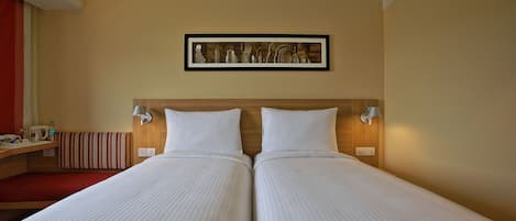 Un lit double avec une tête de lit en bois, deux tables de chevet avec des lampes, un banc rouge et un tableau encadré au mur.