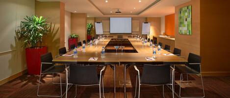 A conference room with a long table, chairs, water bottles, and a projector screen.