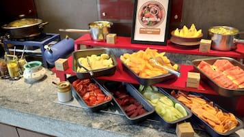 Un bufé con diversos alimentos, entre ellos frutas, verduras y salsas.