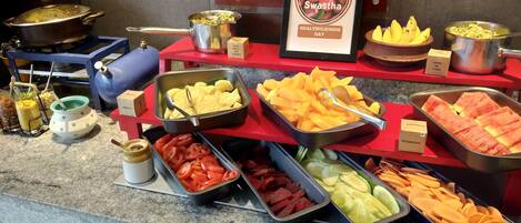 A buffet with various food items including fruits, vegetables, and sauces.
