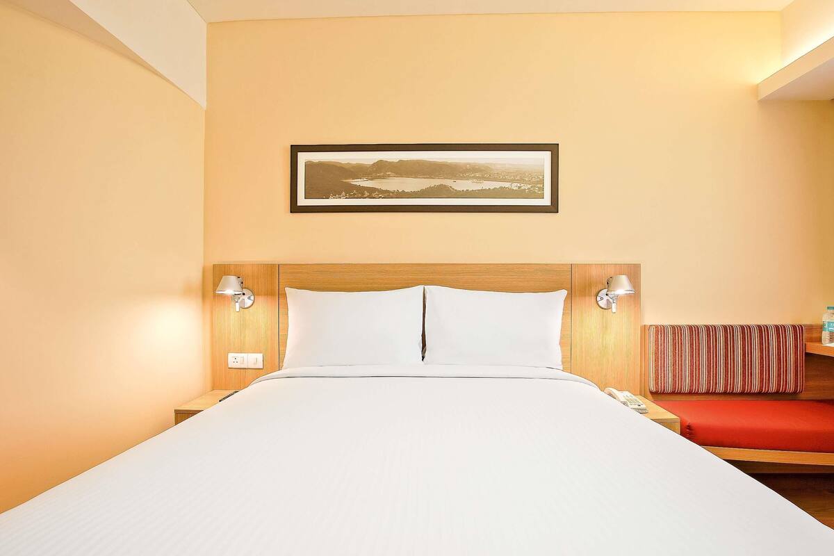 Una habitación de hotel con una cama, un cuadro en la pared y un banco rojo.