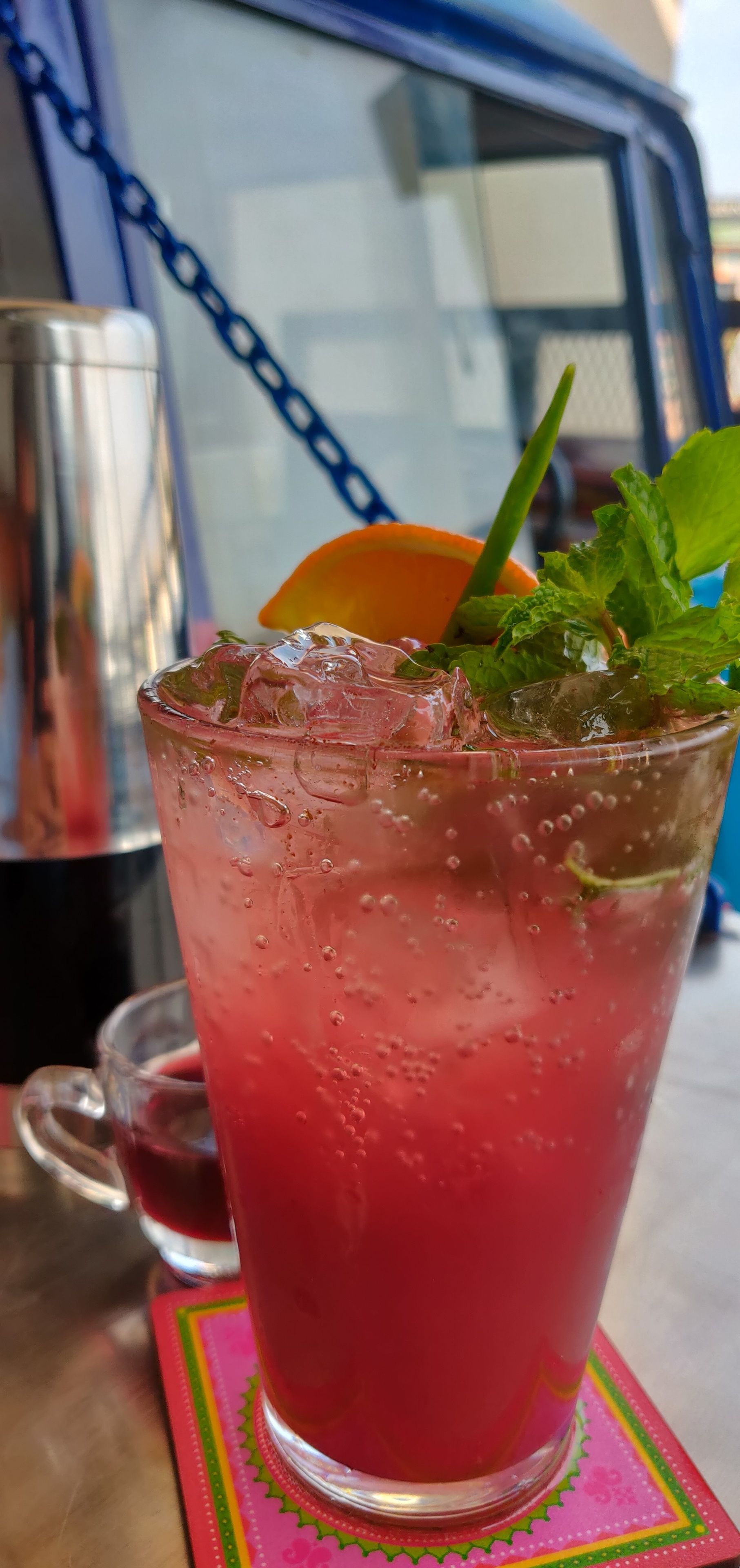 A glass of pink beverage with mint garnish on a coaster.