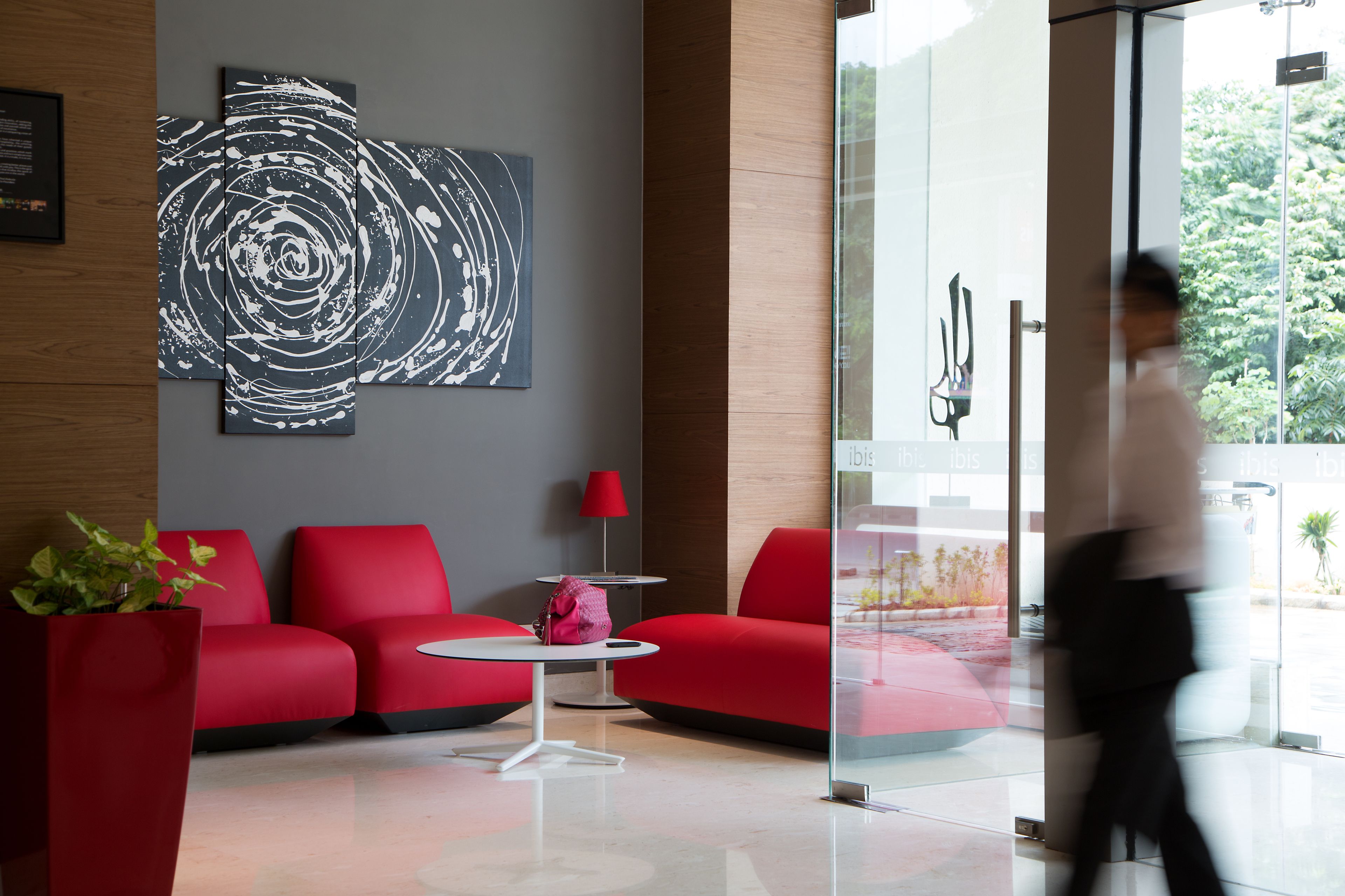 Un vestíbulo moderno con asientos rojos, una entrada con puerta de cristal y un gran cuadro abstracto en la pared.