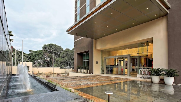 Un edificio moderno con una fuente en primer plano, entrada de vidrio y plantas en macetas.