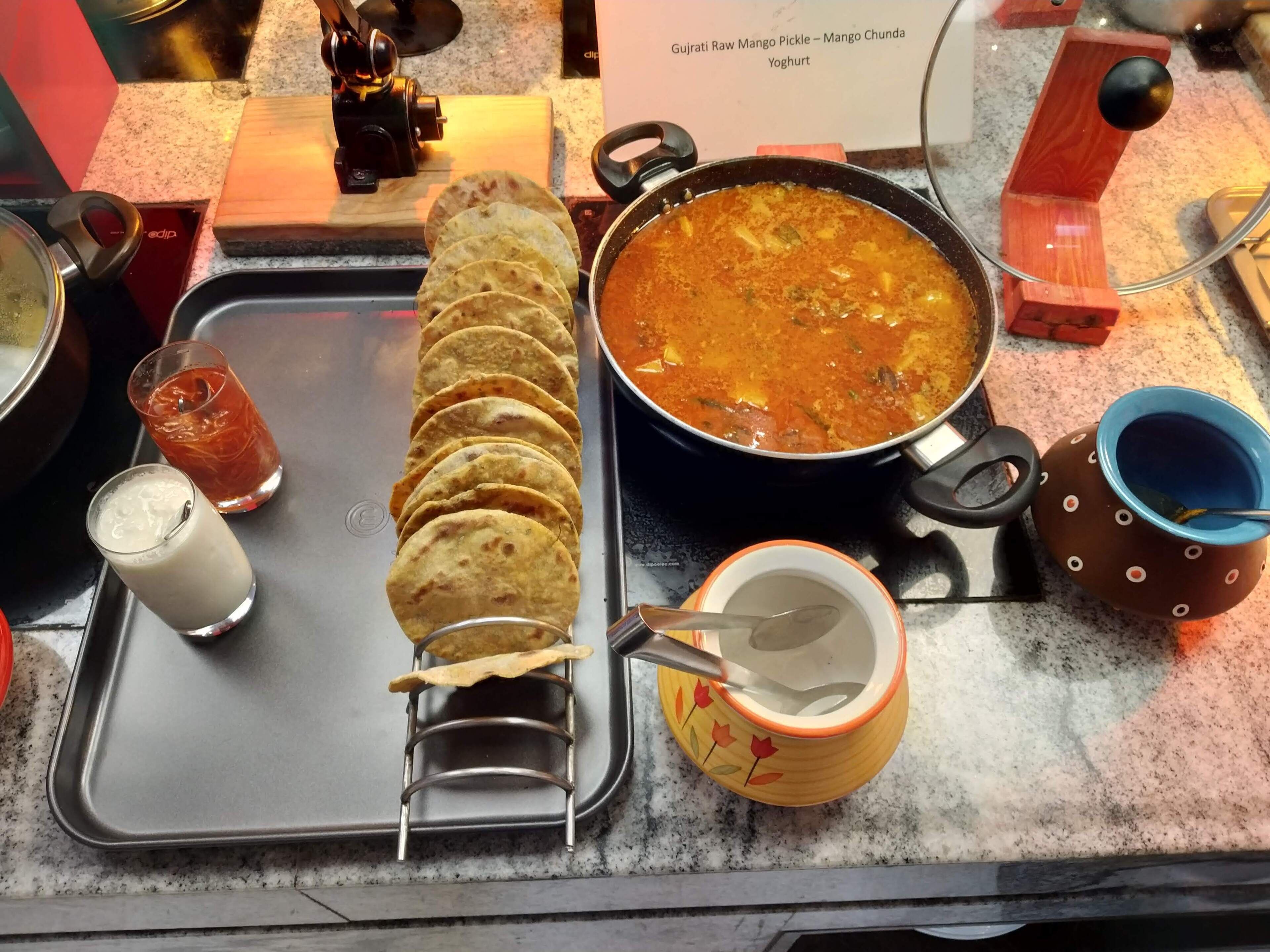 A kitchen counter with a pot of curry, a stack of flatbreads, a glass of milk, and a cup with a spoon.