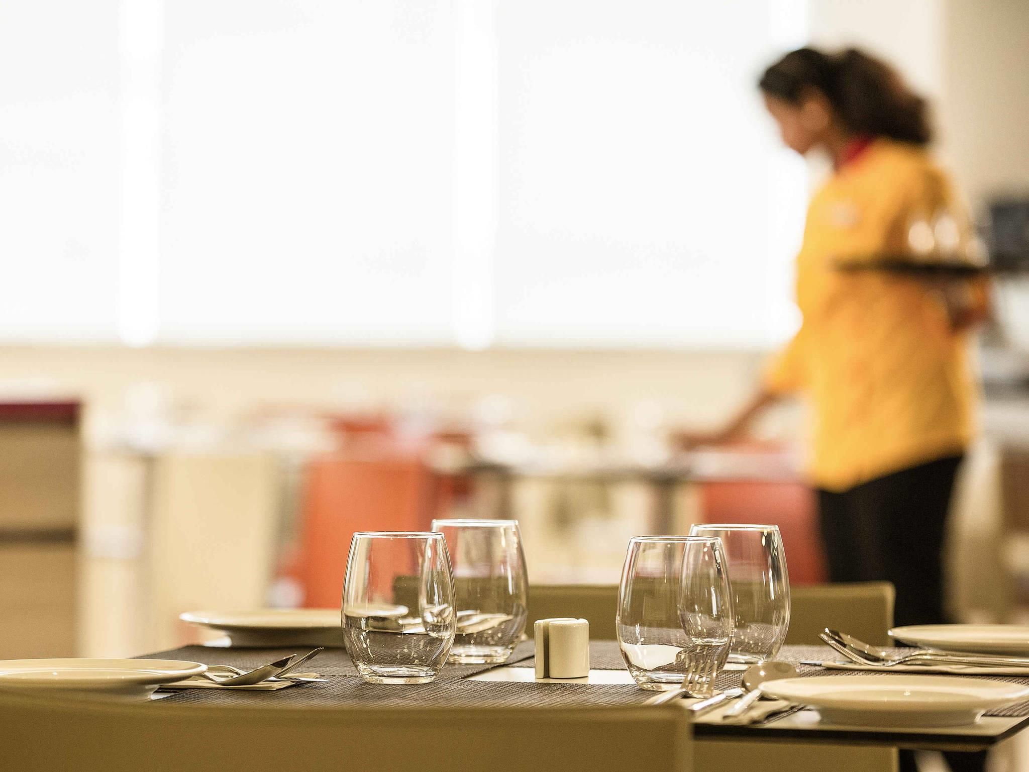 A dining area with tables set for service, a person in a yellow uniform in the background, and a bright interior.