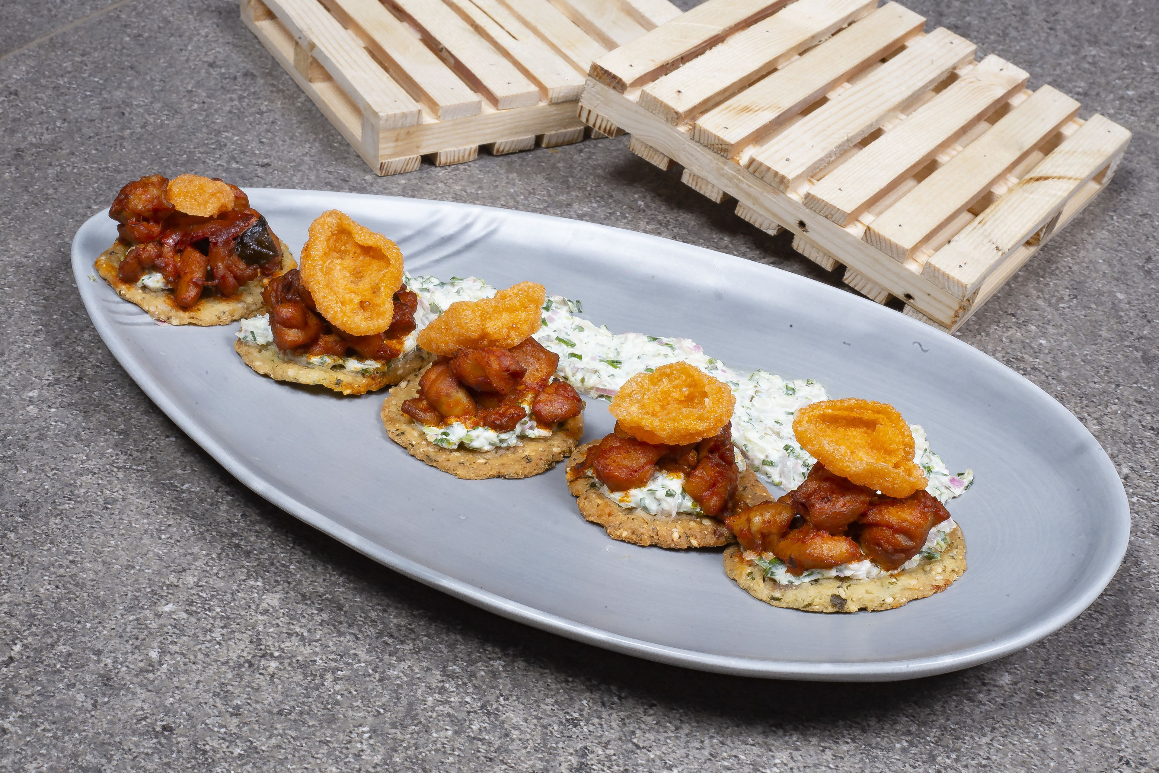 A plate of appetizers with bacon and crackers on a gray plate.