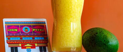 A tall glass of yellow beverage with a frothy top, a colorful card, and a green fruit beside it.