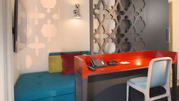 A hotel room with a blue sofa, a red desk, and a white chair.