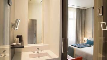 A modern hotel room with a large mirror, a white sink, and a bed with a blue blanket.