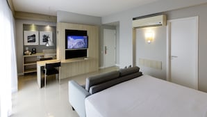 Una habitación de hotel moderna con una cama grande, un escritorio con silla, un televisor de pantalla plana y una pequeña cocina.