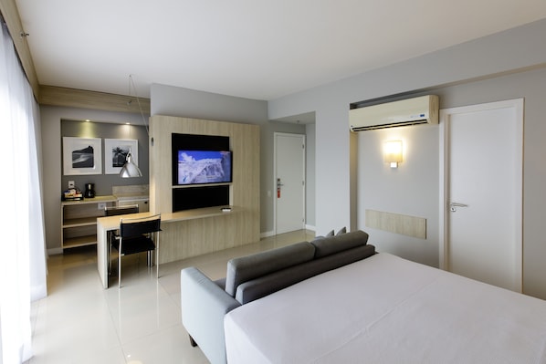 Una habitación de hotel moderna con una cama grande, un escritorio con silla, un televisor de pantalla plana y una pequeña cocina.