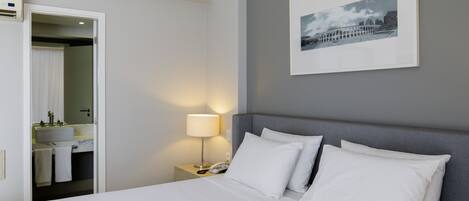 A neatly arranged hotel room with a bed, a bedside lamp, a framed picture on the wall, and a bathroom visible through an open door.