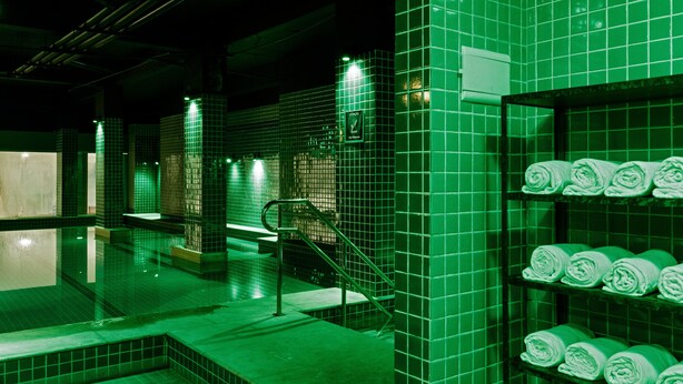 Un baño con paredes de azulejos verdes, una zona de ducha visible y un estante con toallas dobladas ordenadamente.