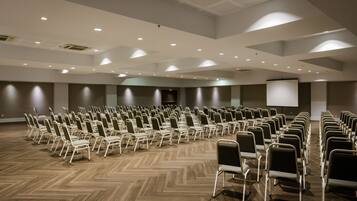 A conference room with rows of chairs, a projector screen, and a wooden floor.