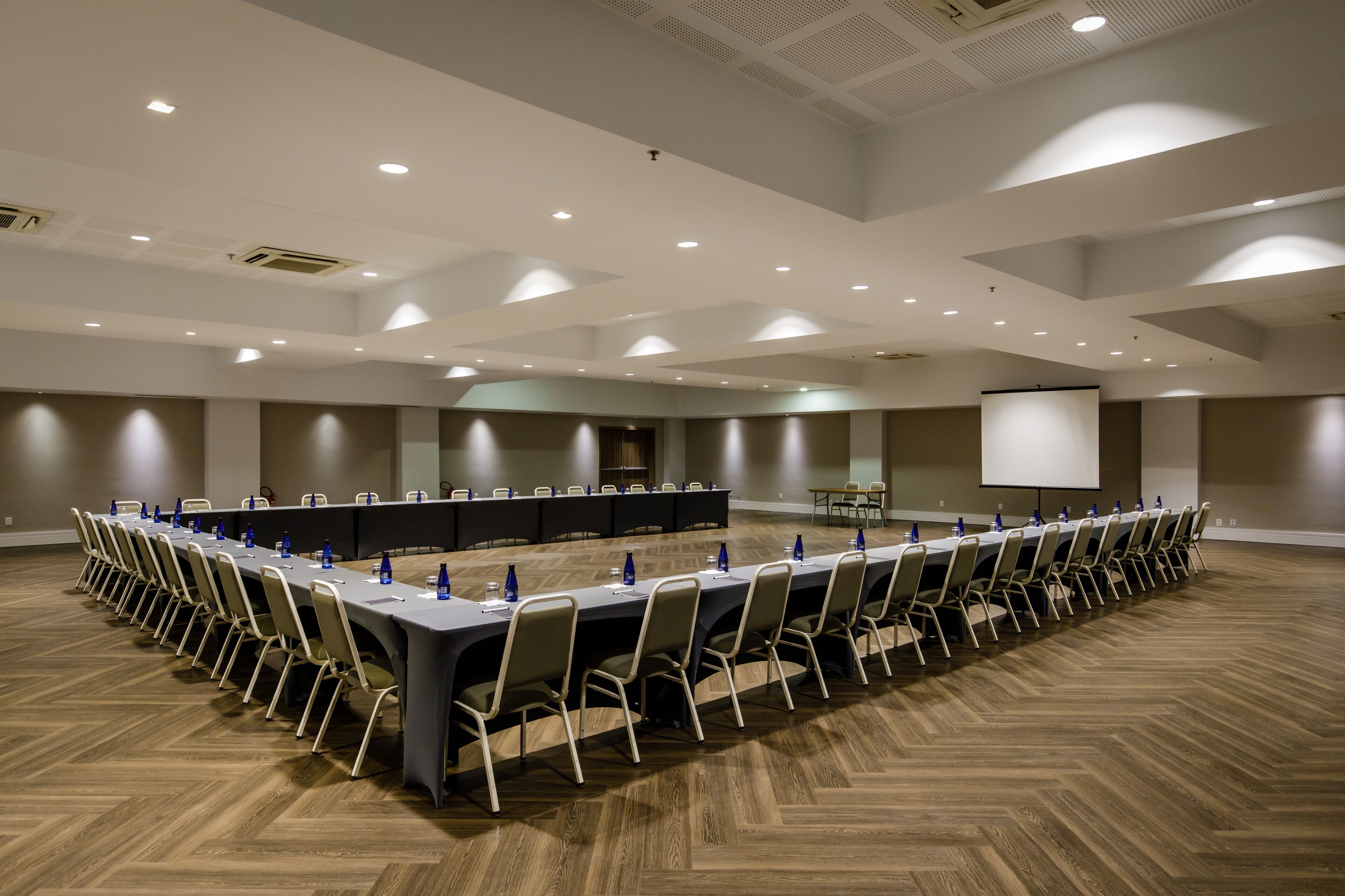 Un salón de conferencias con una larga mesa, sillas y una pantalla para proyector.