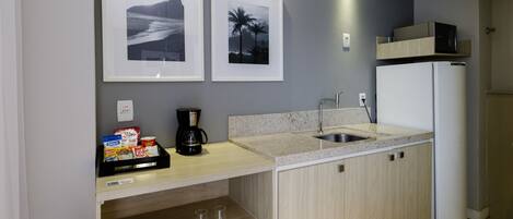 A modern kitchen with a granite countertop, a white refrigerator, and two framed pictures on the wall.