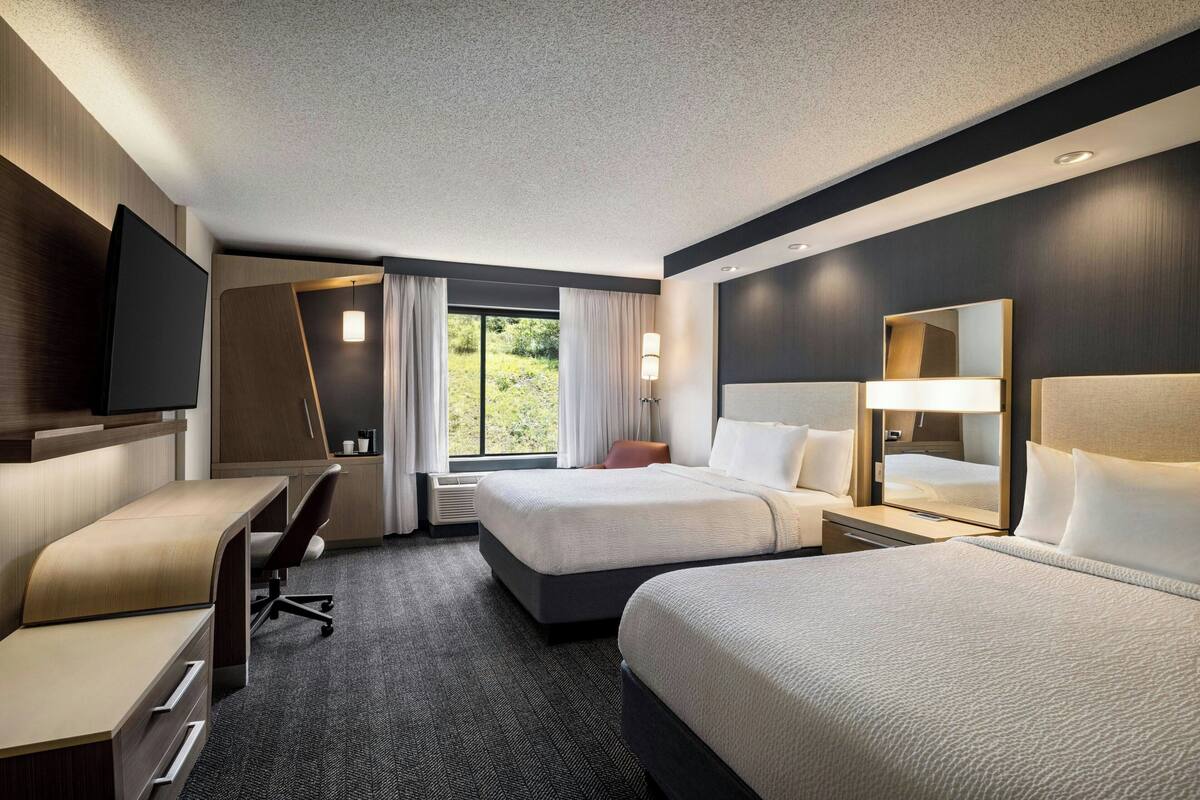 A hotel room with two beds, a desk, a chair, a TV, and a window with curtains.