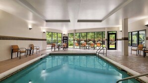 A swimming pool with chairs and tables, surrounded by large windows offering a view of greenery.