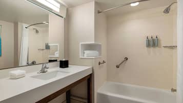 A modern bathroom with a large mirror, two sinks, a bathtub, and a shower.