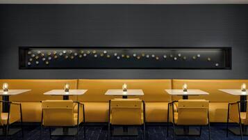 A restaurant with yellow booths and tables, a dark wall with a decorative light fixture, and a patterned floor.