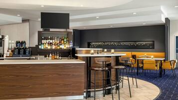 A modern bar area with a wooden counter, stools, and a variety of bottles.