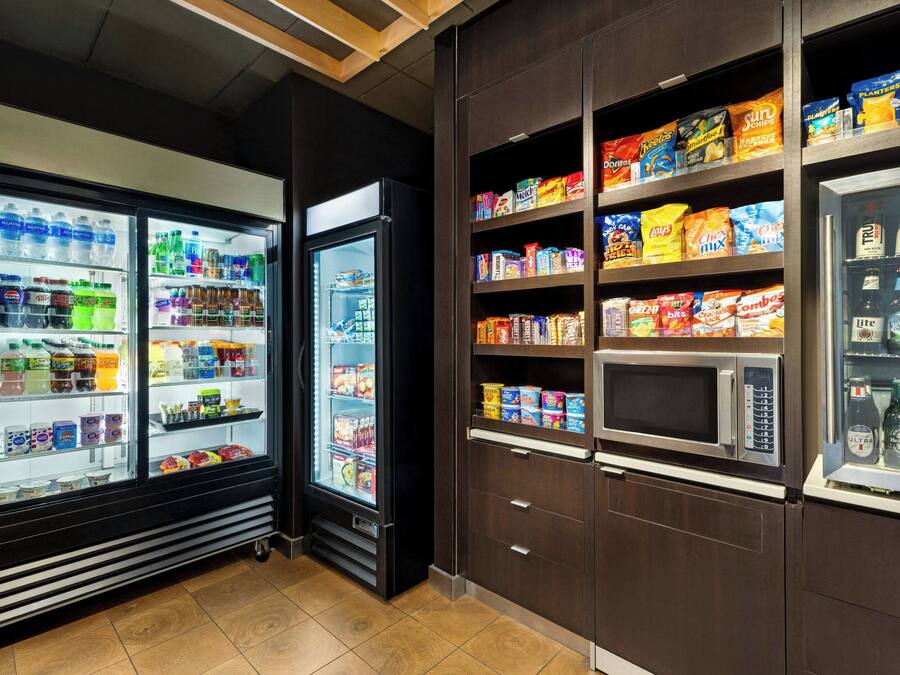 A self-service beverage and snack station with refrigerated drink dispensers and shelves stocked with snacks and bottled beverages.