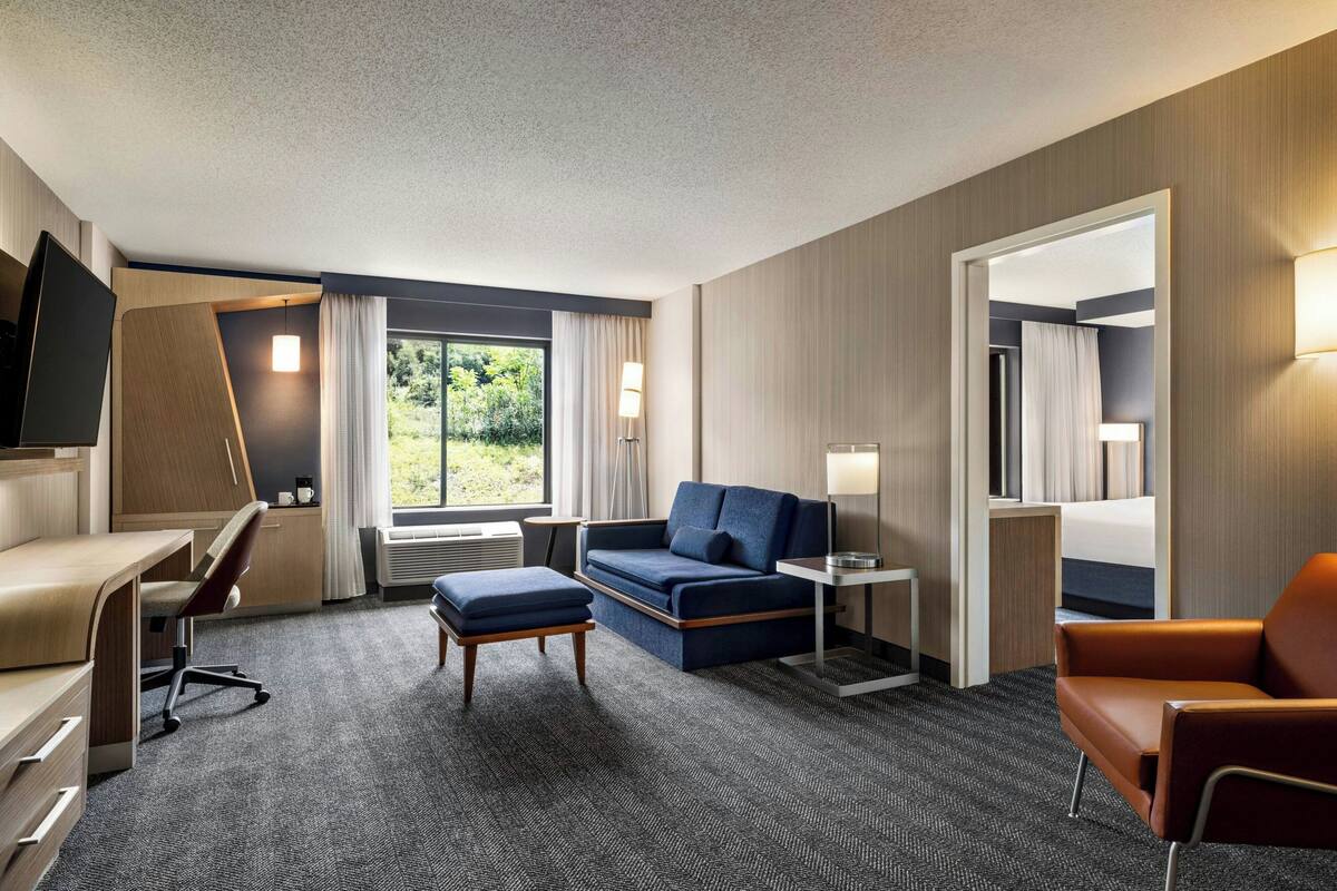 A hotel room with a desk, a sofa, an ottoman, a chair, and a TV.