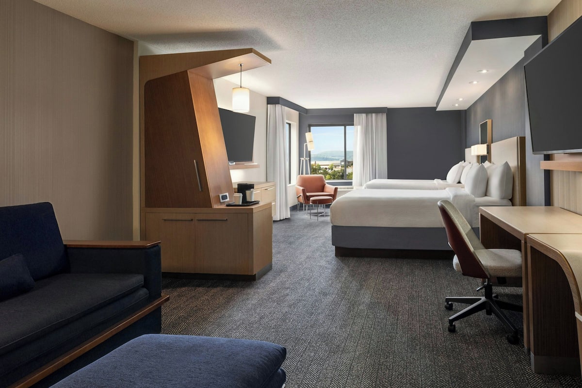 A hotel room with a bed, desk, chair, and a view of the outdoors.