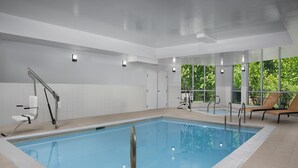 A modern indoor swimming pool with clear glass walls, a lifeguard chair, and a sun lounger by the pool. - Courtyard Philadelphia Bensalem (Bensalem)