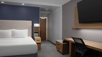 A hotel room with a bed, desk, chair, and a flat-screen TV mounted on the wall.