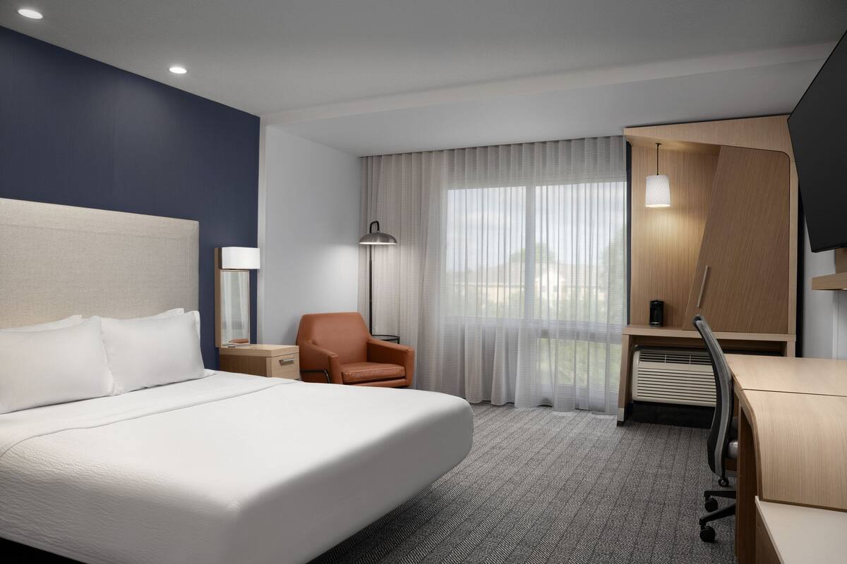 A hotel room with a large bed, a desk, a chair, a lamp, and a TV.