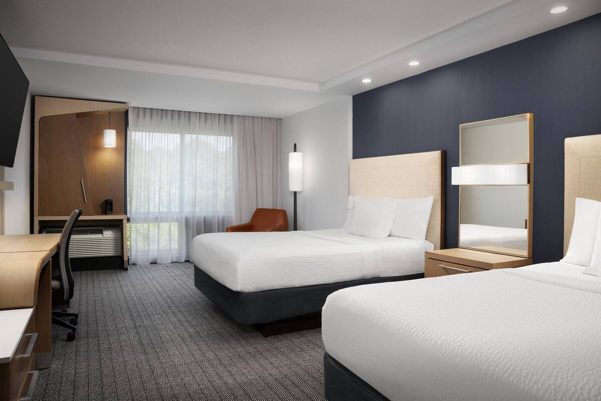 A hotel room with two beds, a desk, a chair, and a large mirror.