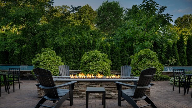 A patio with a stone fire feature, surrounded by Adirondack chairs and a stone table. - Courtyard Philadelphia Bensalem (Bensalem)