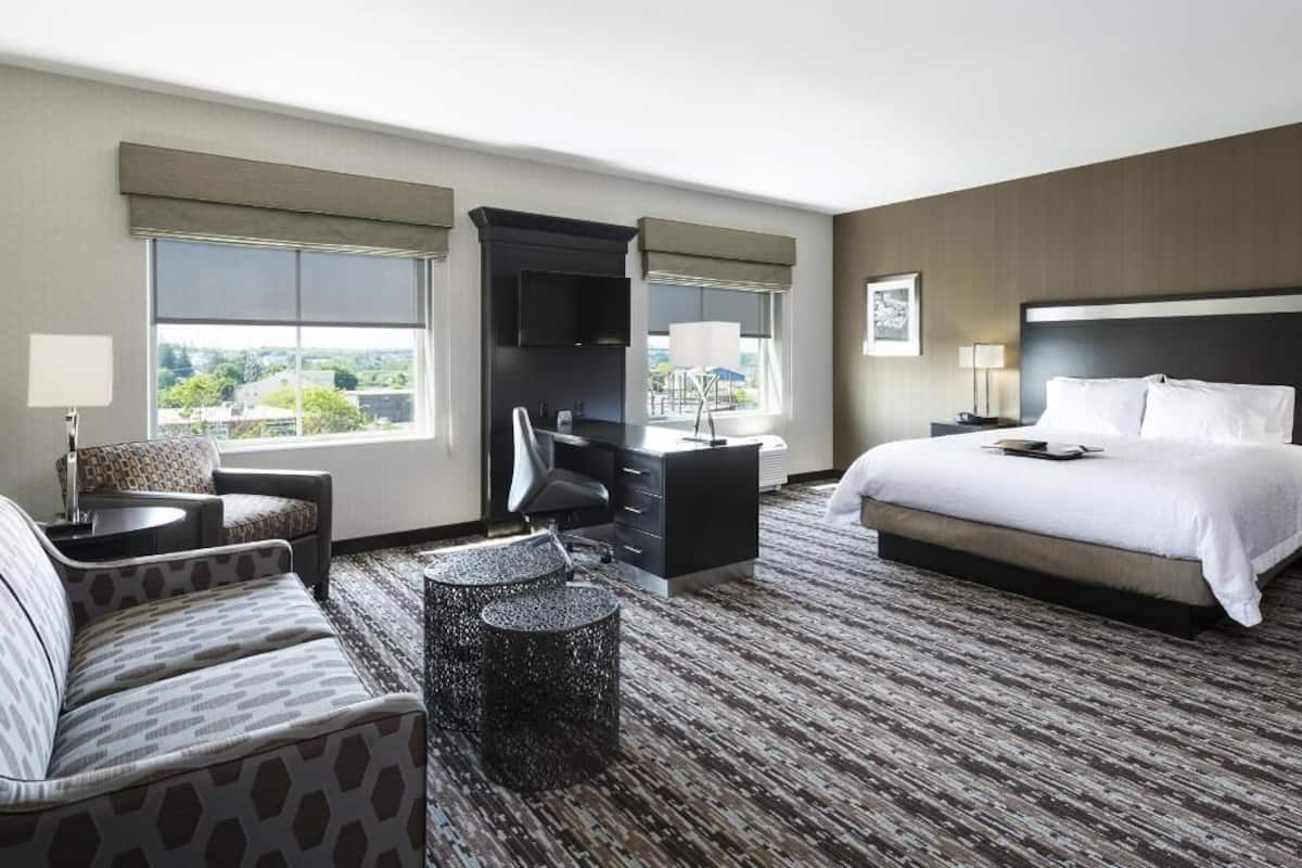Ein Hotelzimmer mit Bett, Schreibtisch, Stuhl, Sofa und Blick ins Freie.