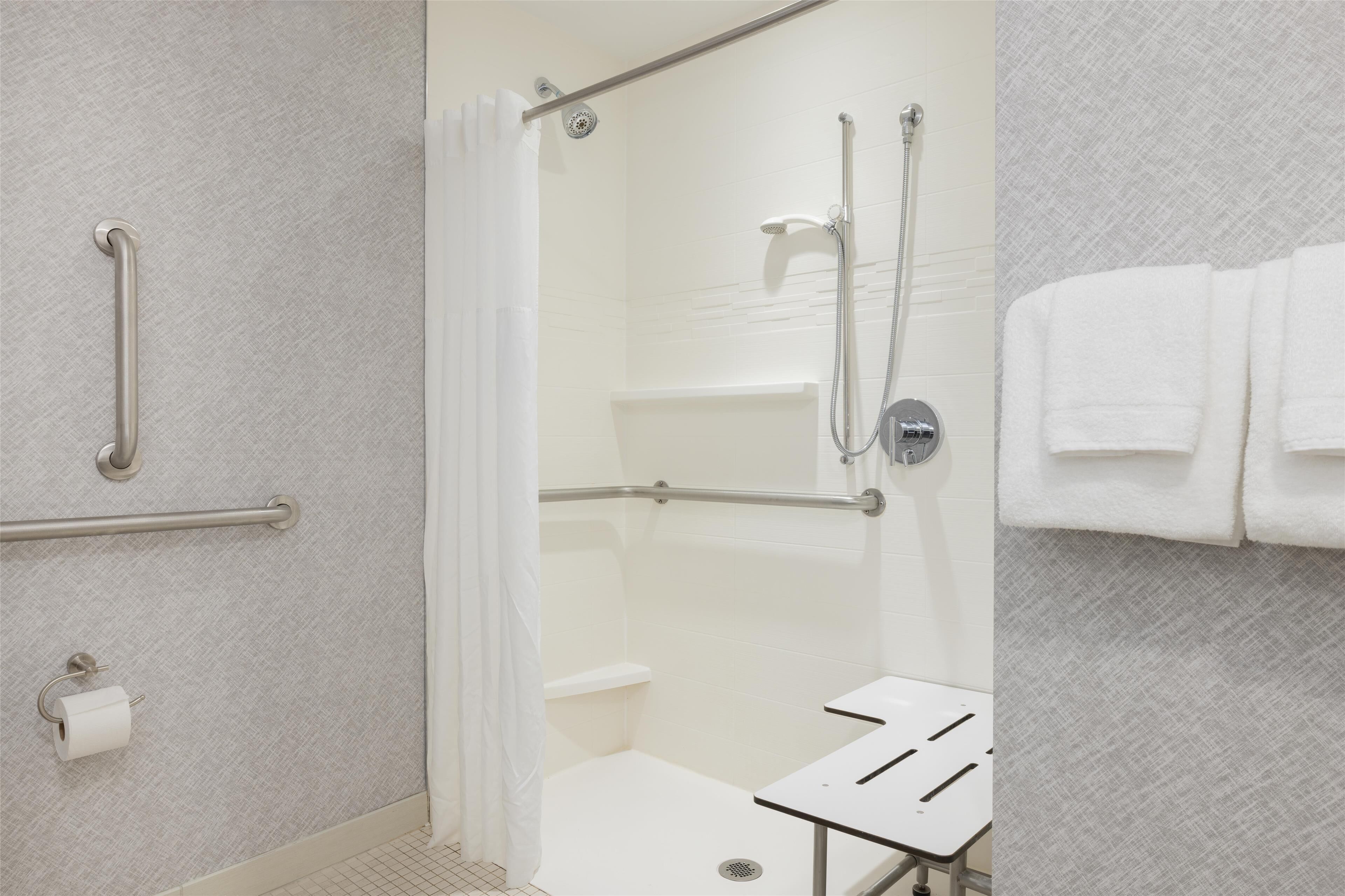 Een moderne badkamer met een inloopdouche, handgrepen, een toilet en een handdoekhouder.