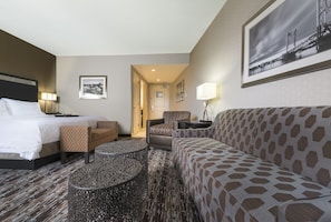 Relax in a stylish room with a large bed, sofa, and armchair, plus a small table and framed artwork.