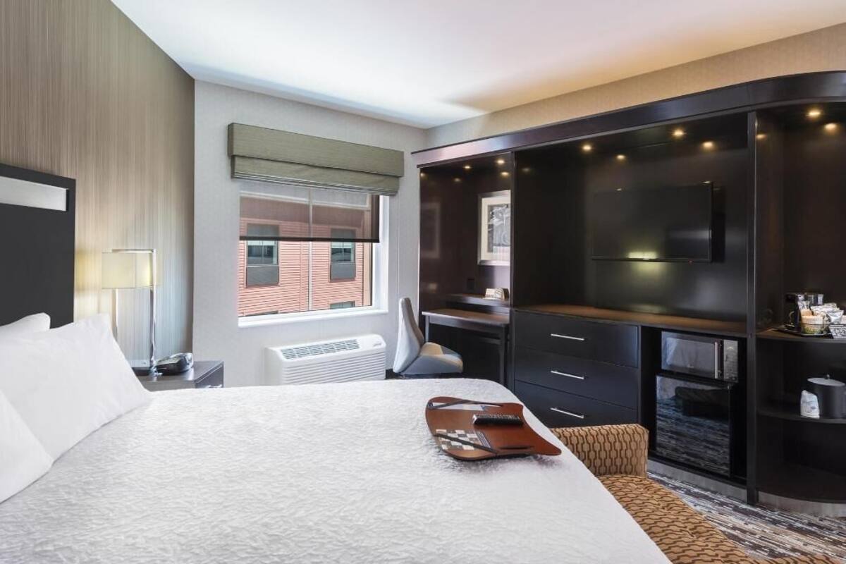 A hotel room with a large bed, a desk, a wardrobe, and a view of the outside.