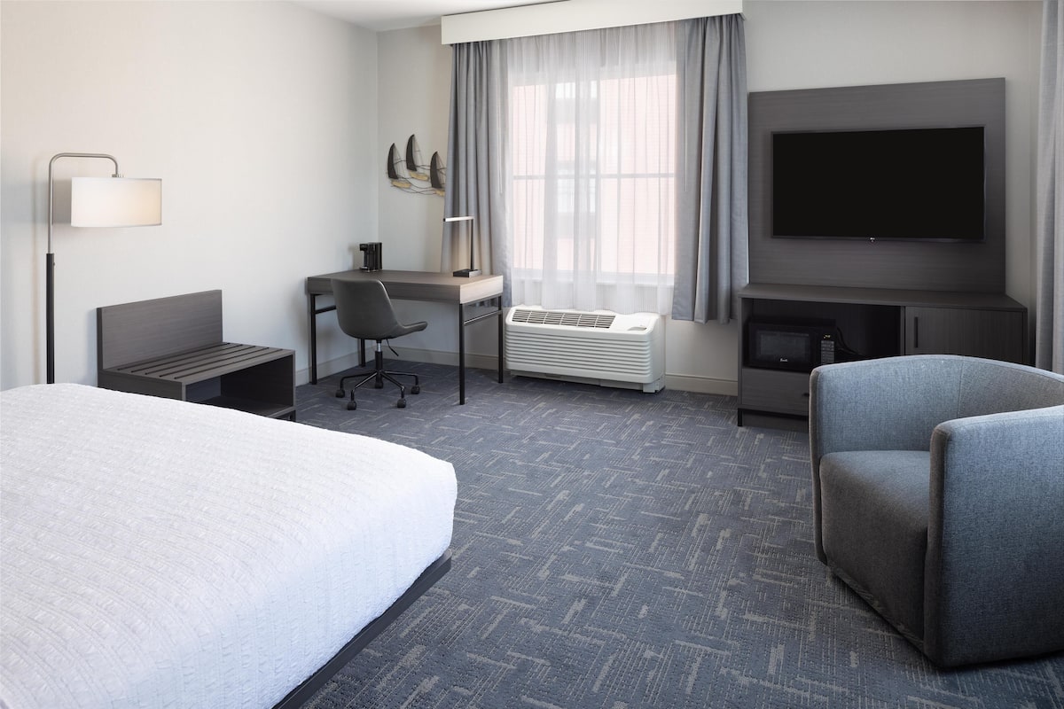 Ein Hotelzimmer mit einem Bett, einem Schreibtisch, einem Sessel, einem Fernseher und einer Heizung.