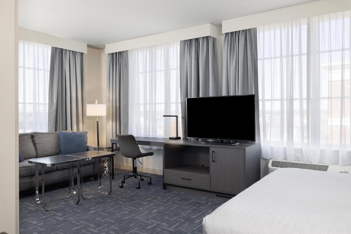 Ein Hotelzimmer mit einem Bett, einem Schreibtisch mit Fernseher, einem Sessel, einer Couch und einer Lampe.