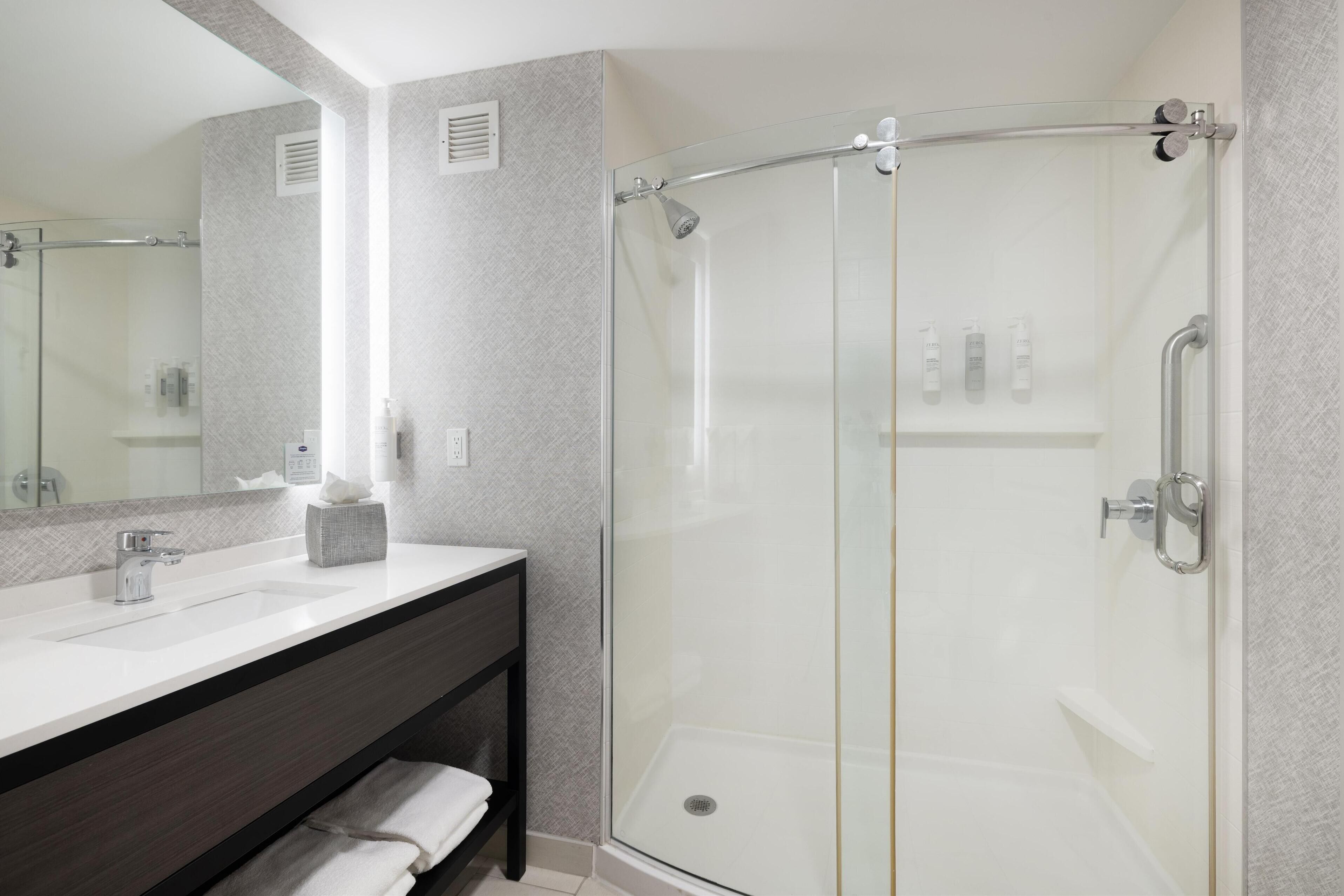 A modern bathroom with a glass-enclosed shower, a vanity with a dark wood cabinet, and a large mirror.