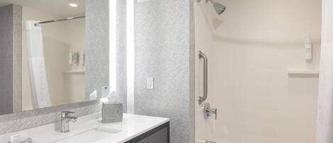 A modern bathroom with a large mirror, a sink, a shower with a handheld showerhead, and a bathtub.
