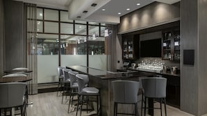 A modern bar area with a glass partition, bar stools, and a counter with glasses and bottles.