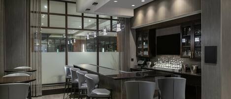 Uma área de bar moderna com divisória de vidro, banquetas e balcão com copos e garrafas.