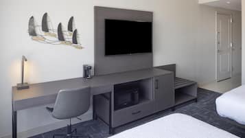 Een moderne hotelkamer met een flatscreen televisie aan de muur, een bureau met stoel, een magnetron en een bed met wit beddengoed.