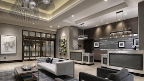 A modern hotel lobby with a reception desk, seating area, and a large window.