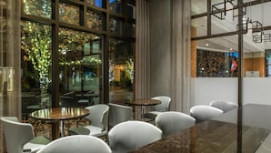 A modern indoor space with glass walls, multiple seating areas, and a view of an outdoor garden with lights.
