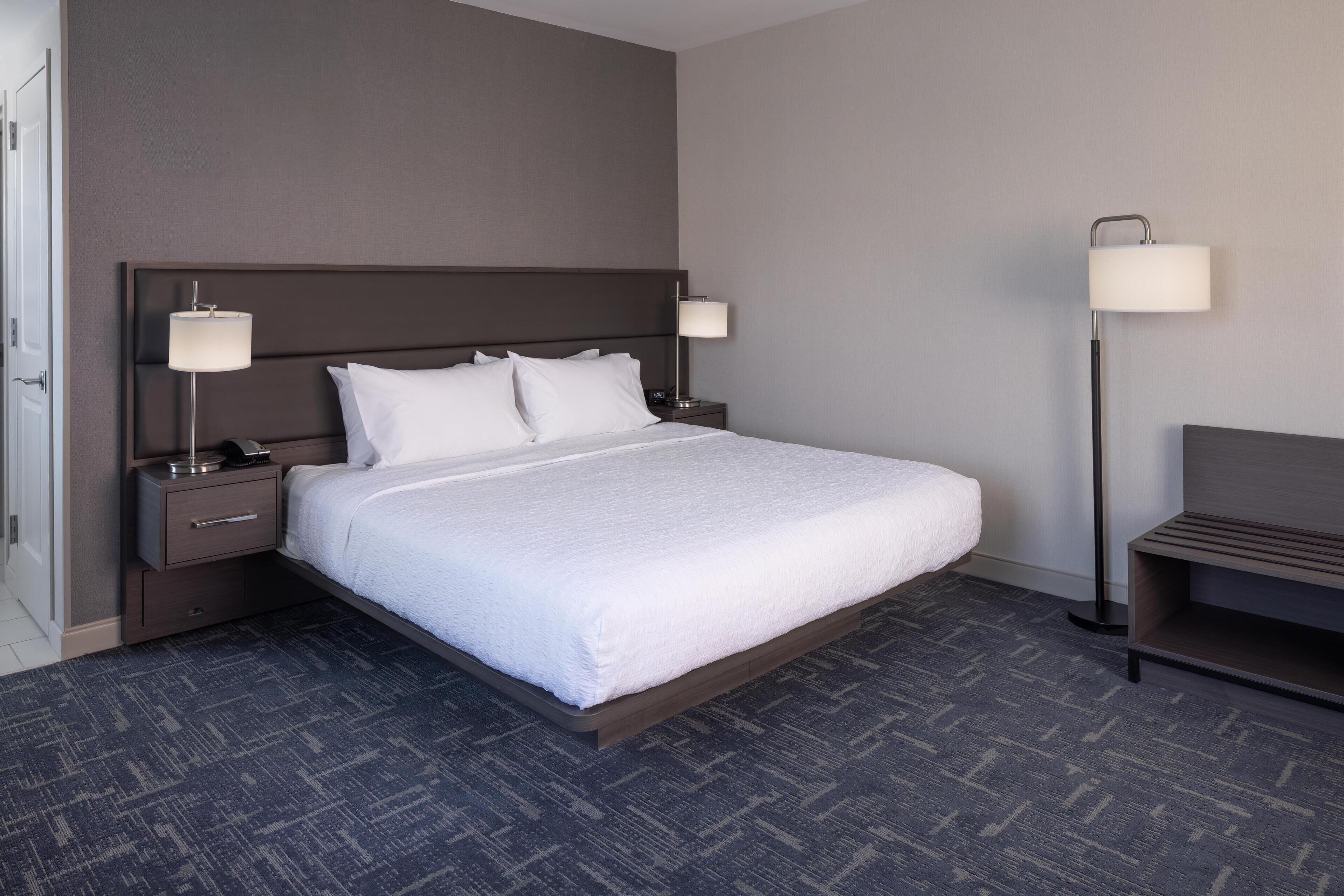 A neatly made hotel room with a large bed, two bedside tables with lamps, a nightstand, and a bench.